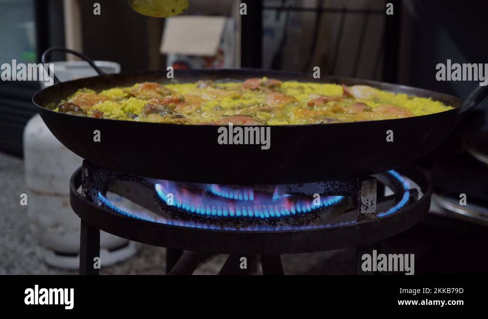 Checking On Spanish Paella With A Spoon While Cooking On A Stove With