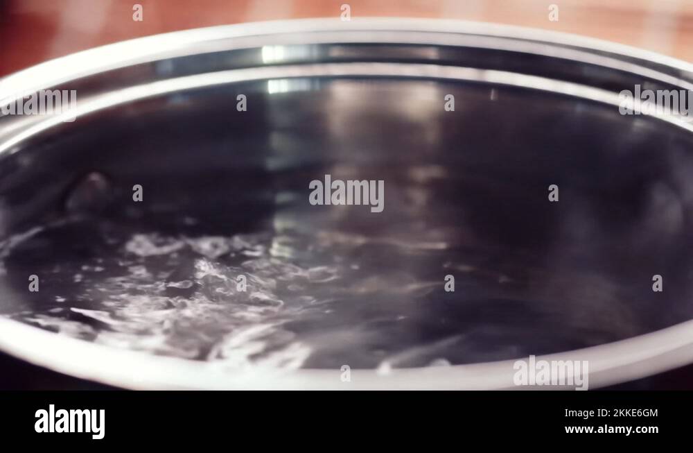 Boiling water in a cooking pot on kitchen stove, hot steam rising from ...