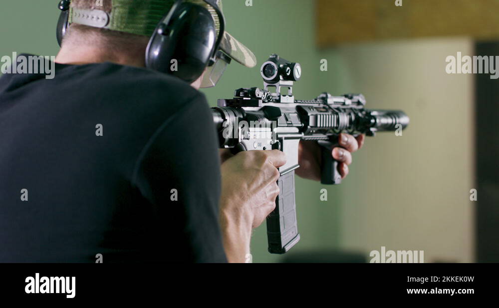 Back view of a man wearing ear protection shooting a rifle in an indoor