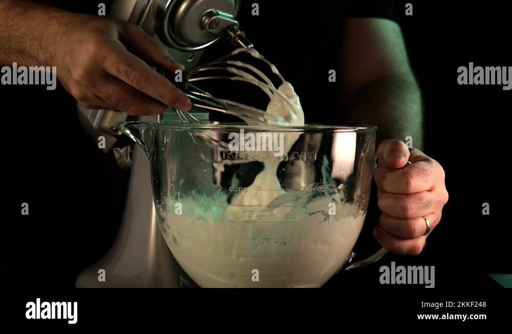 Kitchen Aid stand mixer whipping cream in a glass bowl with man's hand