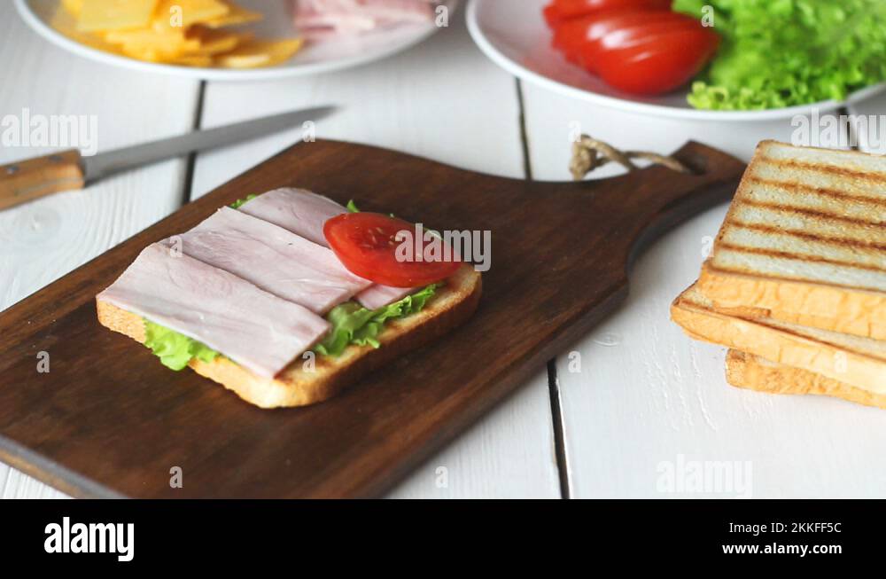 The process of making a sandwich with salad, tomato, ham and cheese