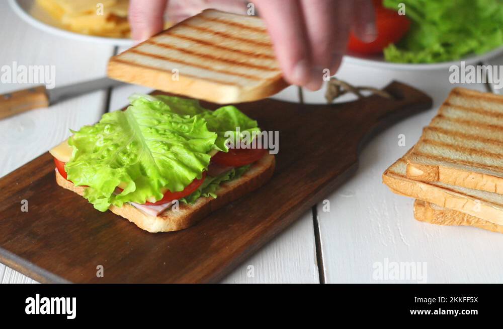 The process of making a sandwich with salad, tomato, ham and cheese