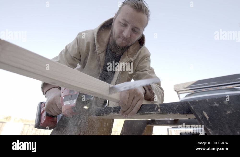 Young craftsman uses reciprocating saw to cut through wooden plank