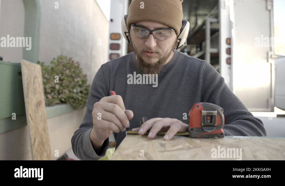 Craftsman wearing safety glasses and ear muffs marks timber with pen