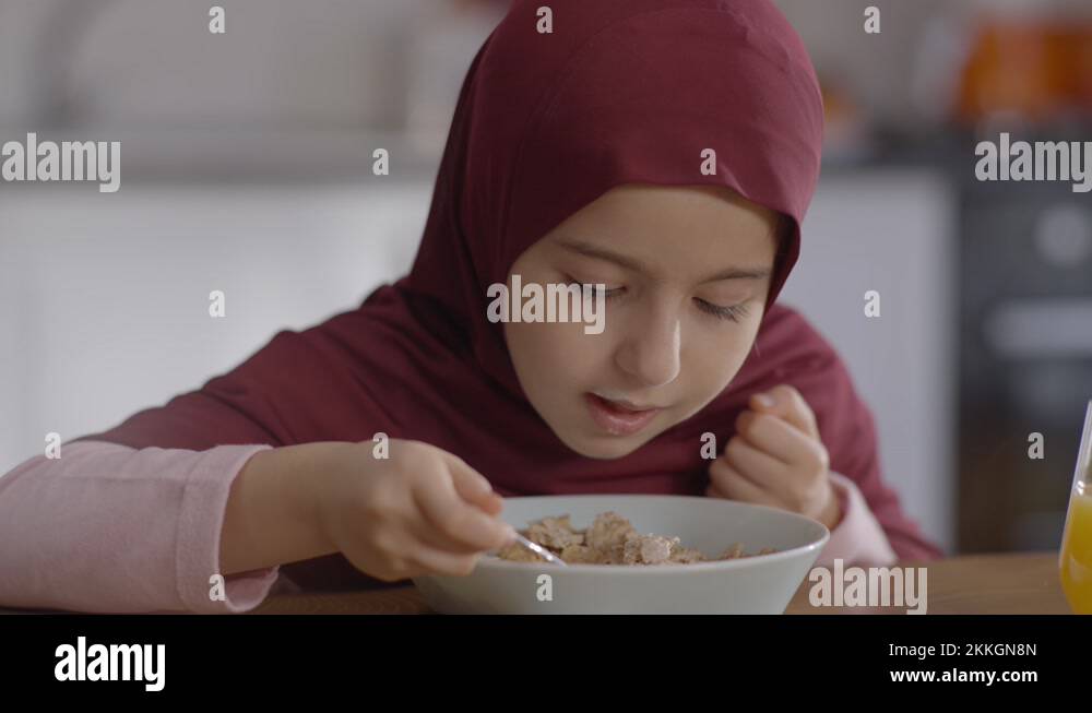 Muslim girl in hijab eating healthy granola grains with milk from bowl
