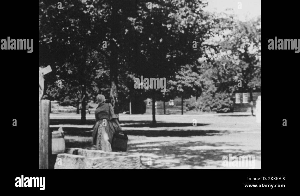 1950s People get water from well. House. Man lifts bucket. Woman works