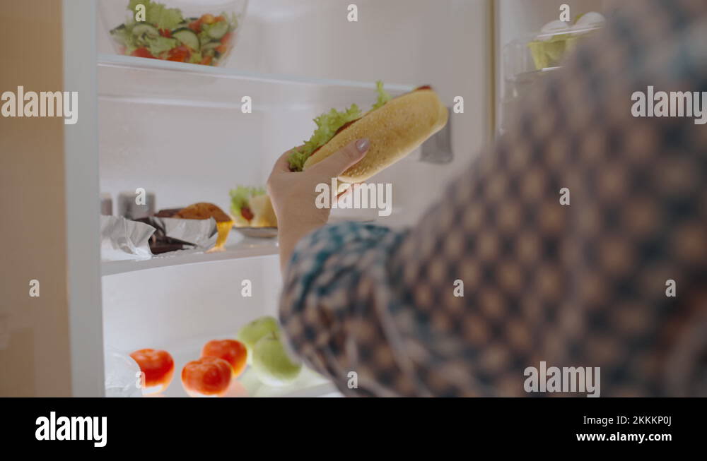 Addicted plump woman taking hot dog from the fridge in kitchen, weight
