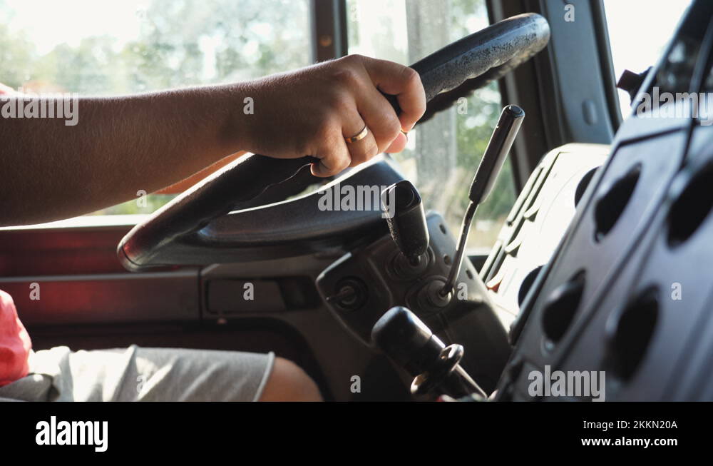Male arms of lorry driver holds a big steering wheel while operating a