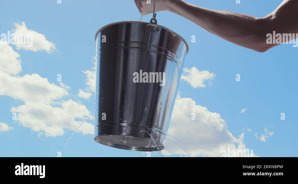 Man lifts Leaking bucket with water dripping, blue sky clouds, Lost