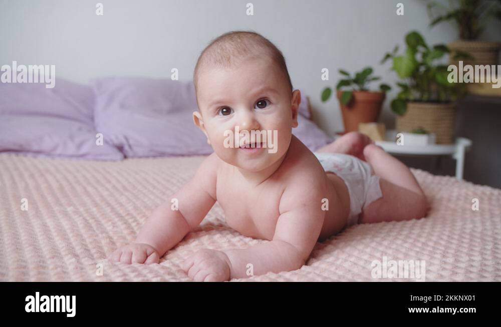 Newborn baby smiling at the camera lies on its stomach on the bed at