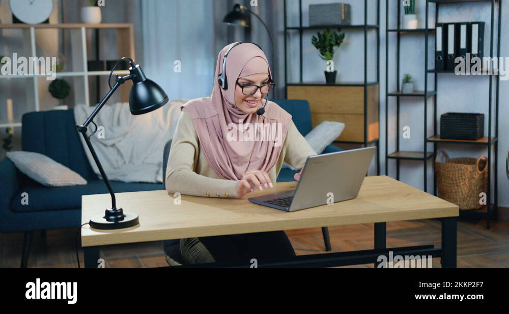 Attractive happy smiling young arabic woman in hijab sitting in front ...