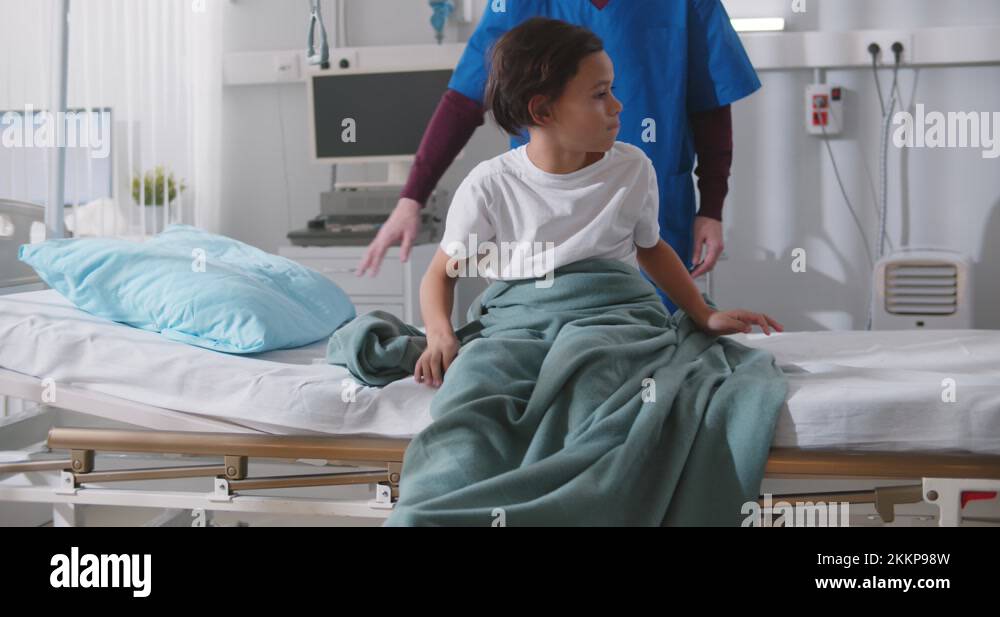 Male nurse helping african boy patient lying down in bed and falling