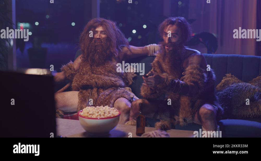 Ancient neanderthal couple of cavemen watching TV curiosly interacting ...