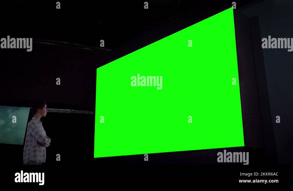 Woman looking at large blank green screen in dark room chroma key concept Stock Video Footage