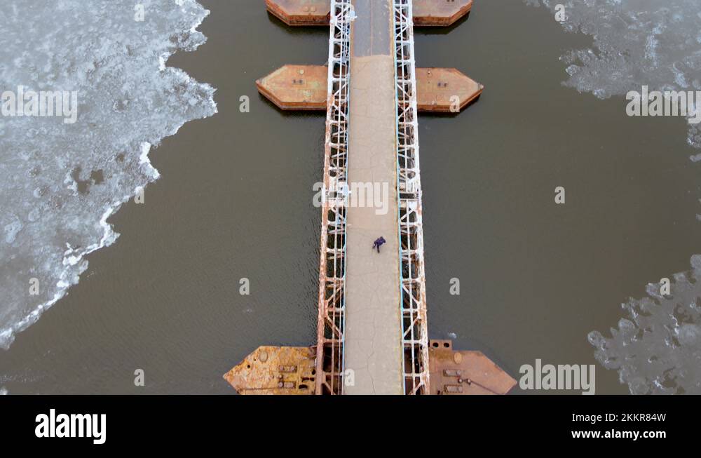 Steel pedestrian pontoon bridge with lanterns through river with