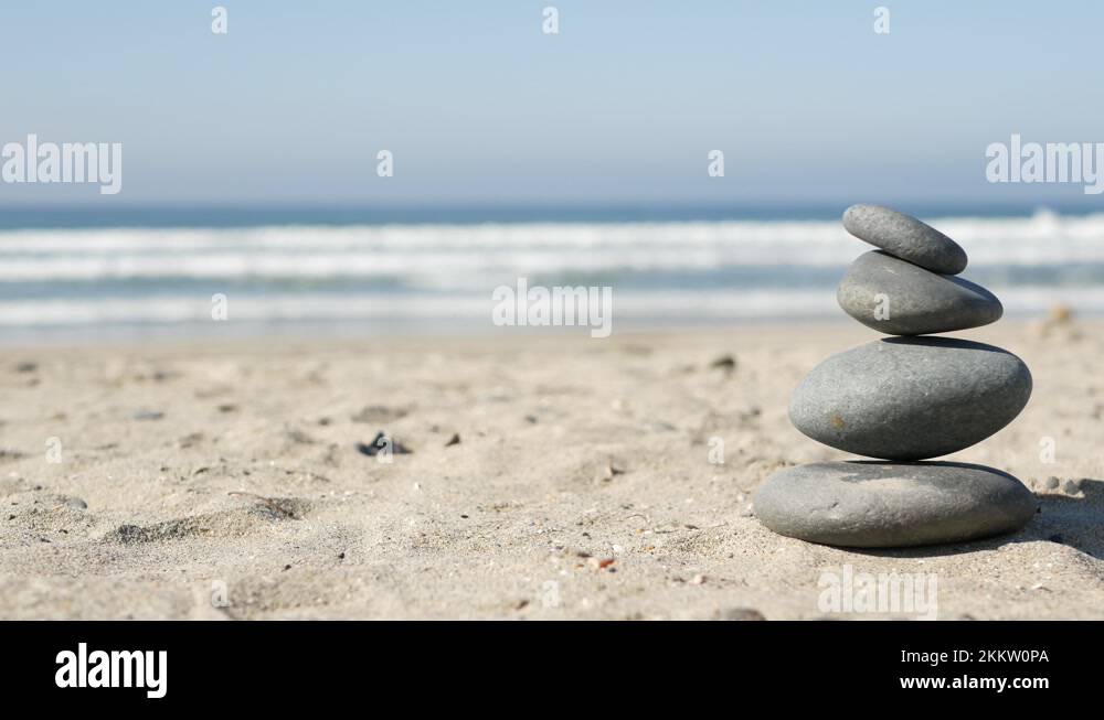 Rock balancing on ocean beach, stones stacking by sea water waves ...