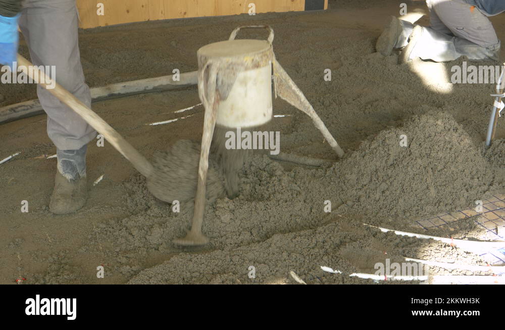 CLOSE UP Workers spread wet cement across the ground of an unfinished