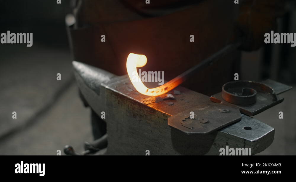 Blacksmith hits with a hammer and shapes the redhot metal on the anvil