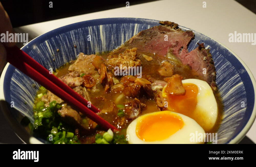 Chopsticks eating beef broth ramen noodle soup with fried garlic green