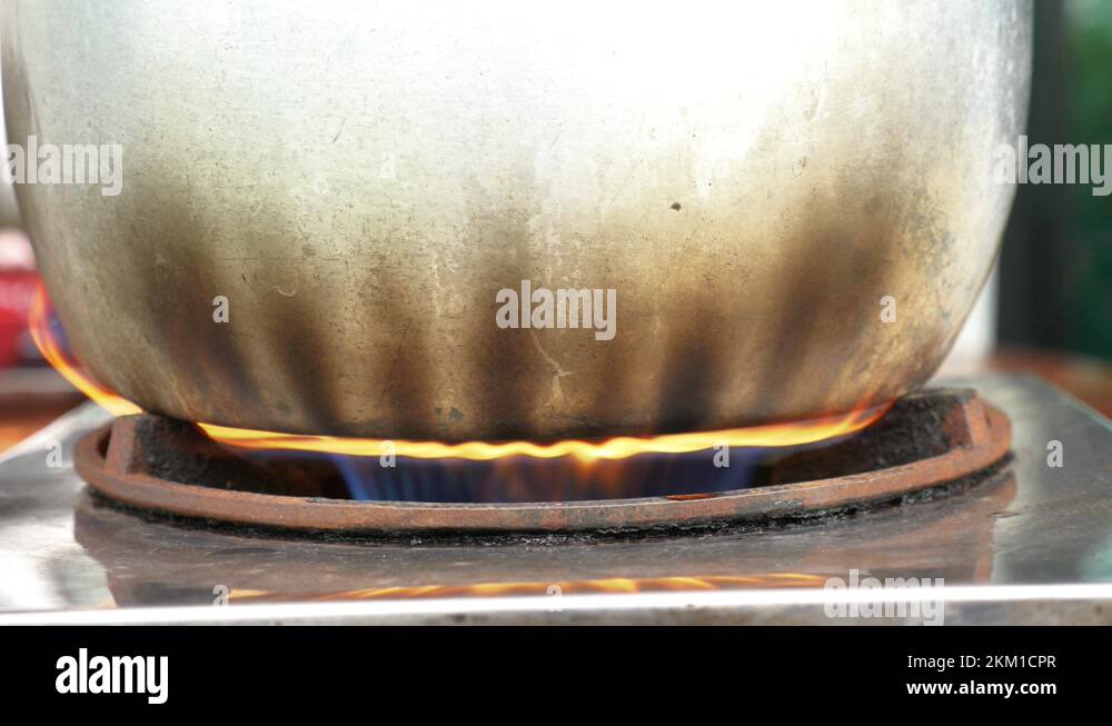 Stainless steel pot with burnt sides on boiling water on fire, handheld