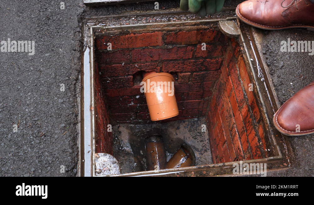 Inspecting drain sewer man with gloves on points to problem at open ...
