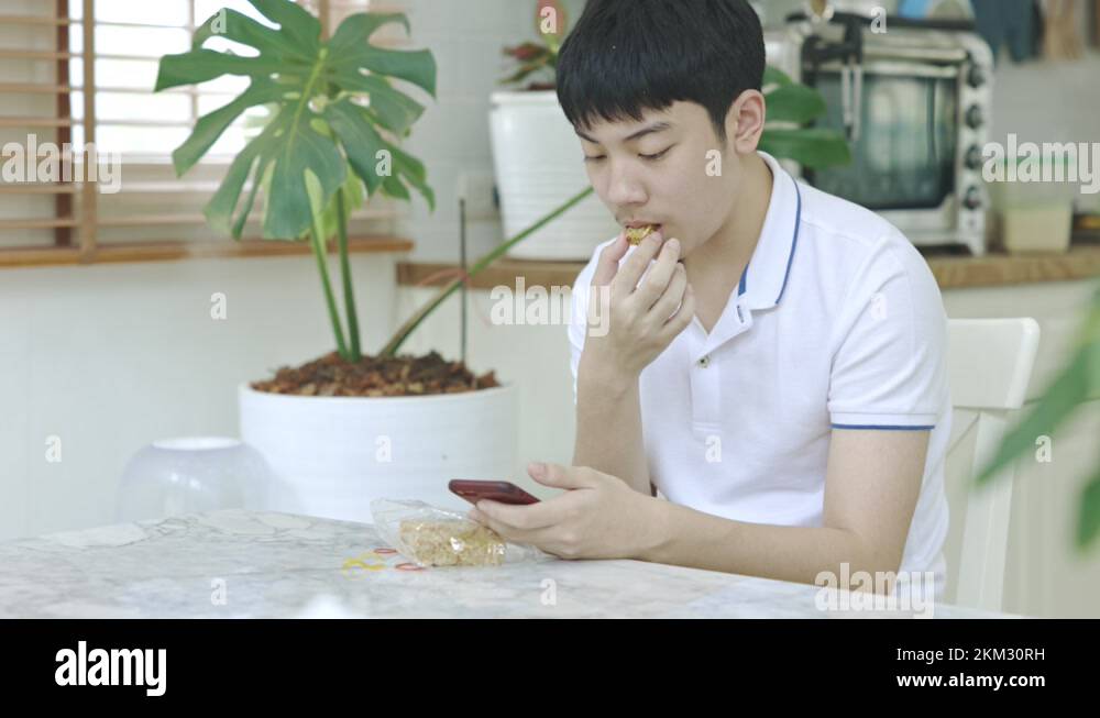 Asian teen boy eating snacks While using the phone at the same time ...