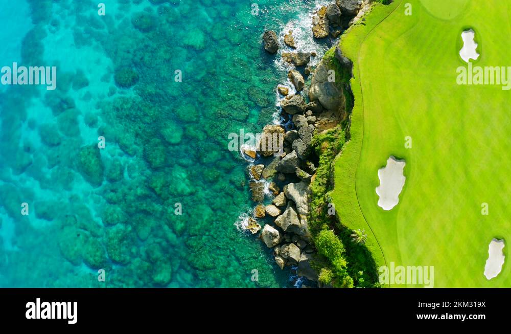 Golf course with green grass and sand traps and blue ocean with coral