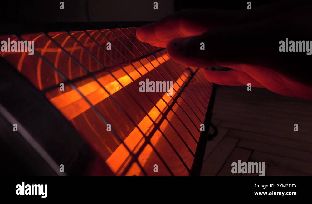 Man warms his hands over an infrared heater in a room in cold weather