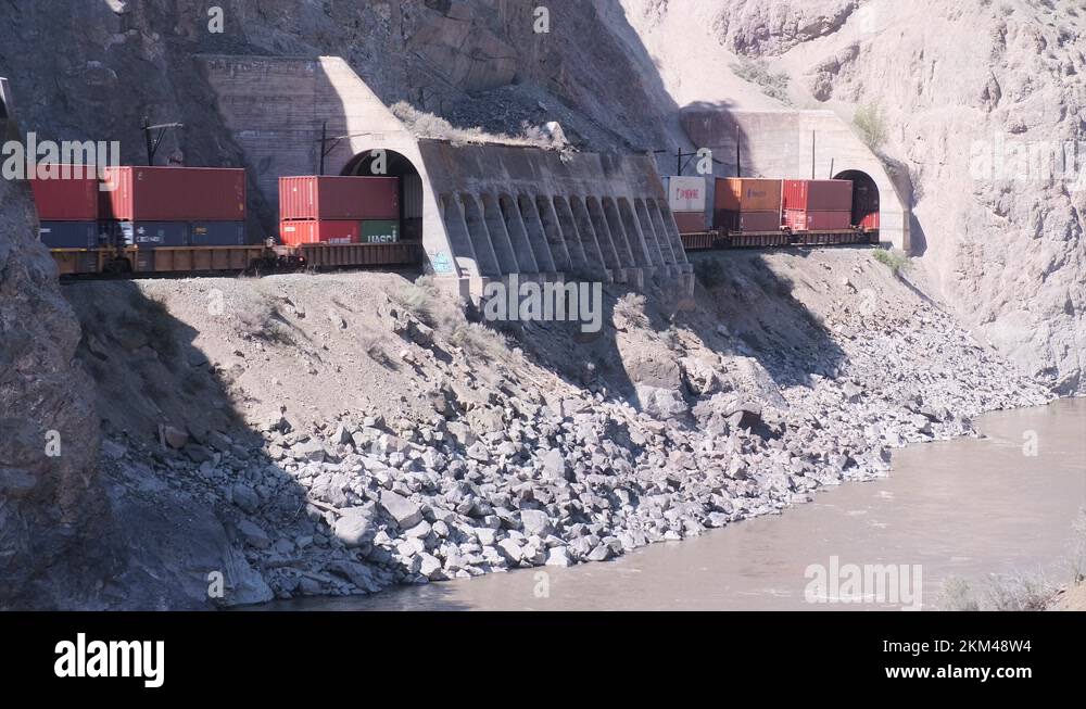 Container cars on freight train pass through rocky riverside tunnels