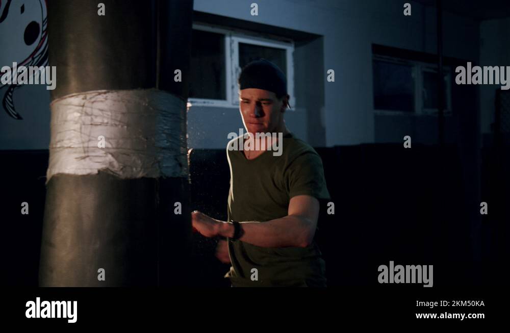 Alone boxer hits punching bag in dark gym in slow motion. Young man ...