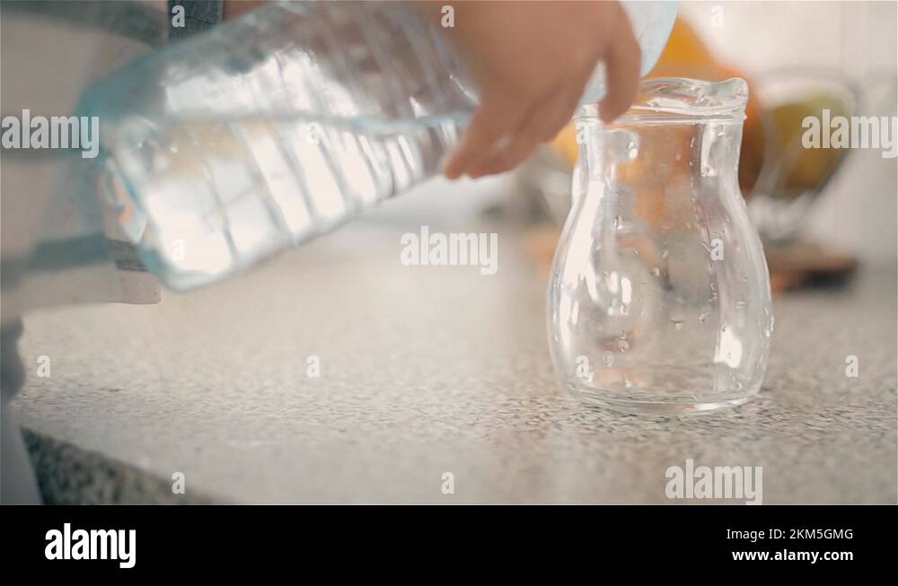 The boy pours from a plastic bottle into a jug of clean drinking water