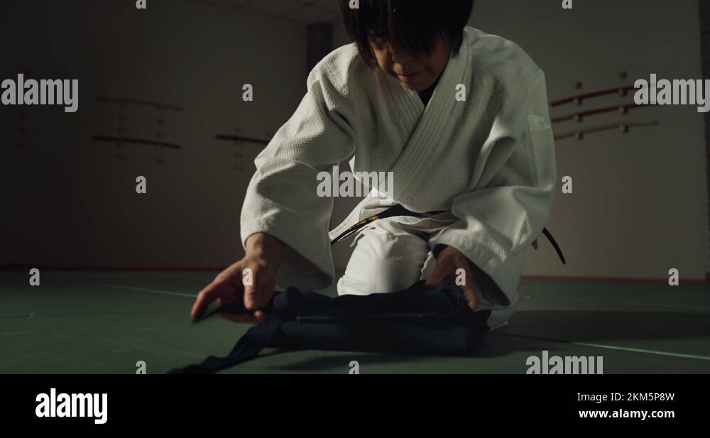 Mature female fighter folding hakama before practicing in martial arts