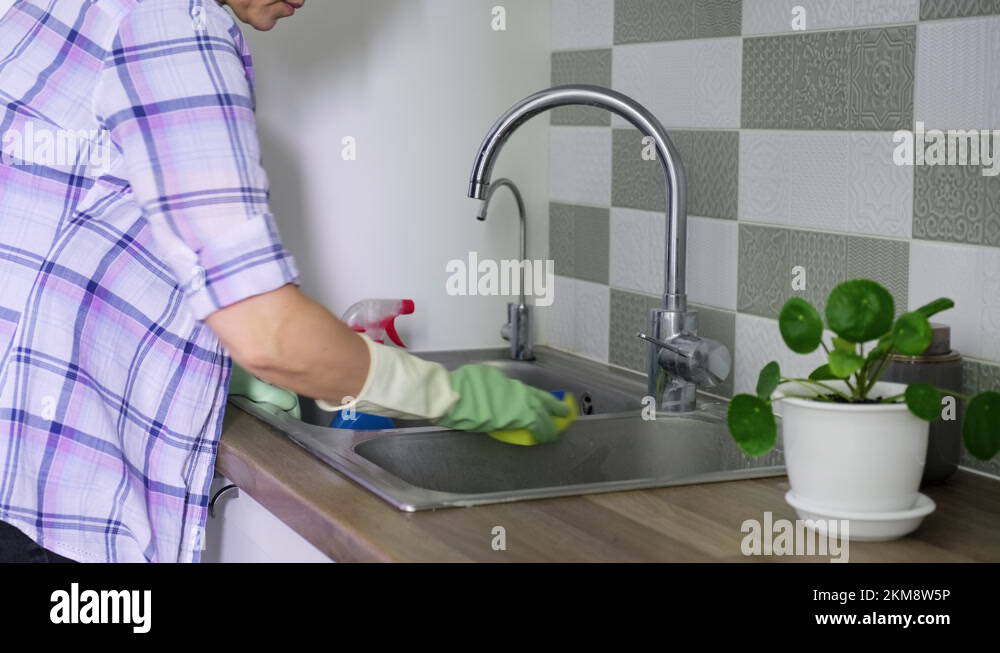 Woman cleaning double chrome sink in rubber gloves using spray and