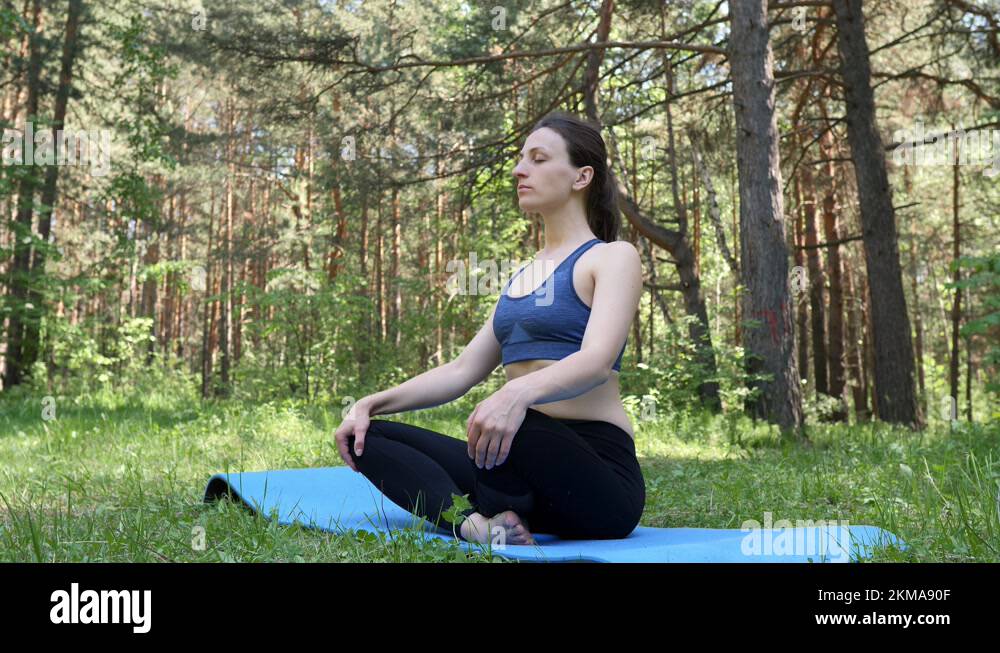 Slender young woman sitting on a yoga mat in a lotus position in a city ...