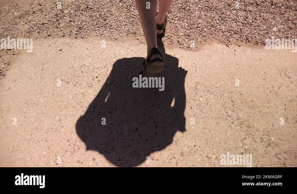 Man's Feet Wearing Sandals Walking On Gravel Path Under The Sun