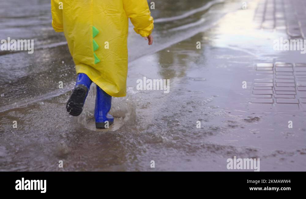 A happy child runs in a puddle in rubber boots and a raincoat. The kid ...