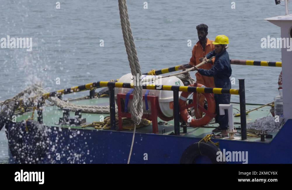 Tugboat Deckman Reaches For Mooring Line Of A Docking Ship With A Hook