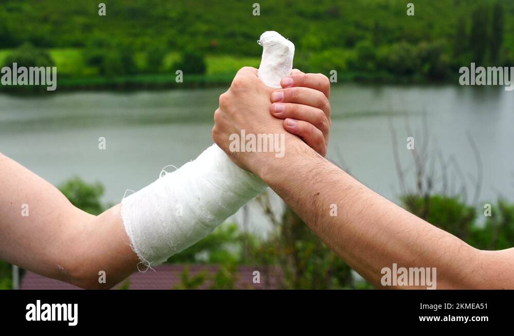 Handshake of two men on nature background. One male hand in a plaster