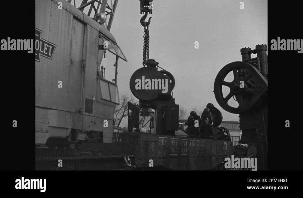 1940s Rail mounted crane lifts a heavy metal object from a railcar