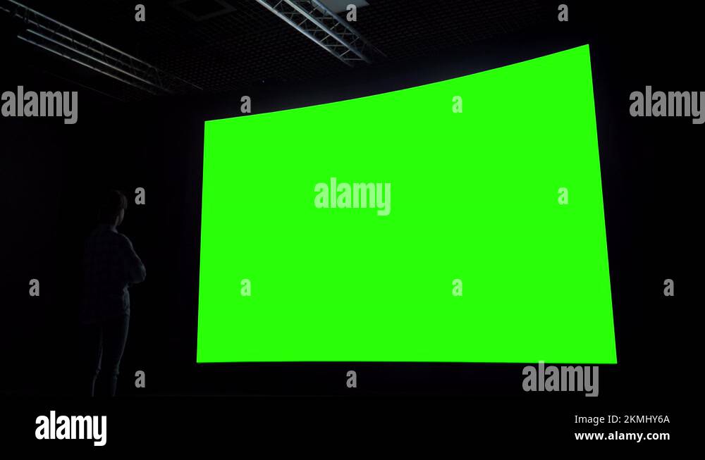 Woman looking at large blank green screen in dark room chroma key concept Stock Video Footage