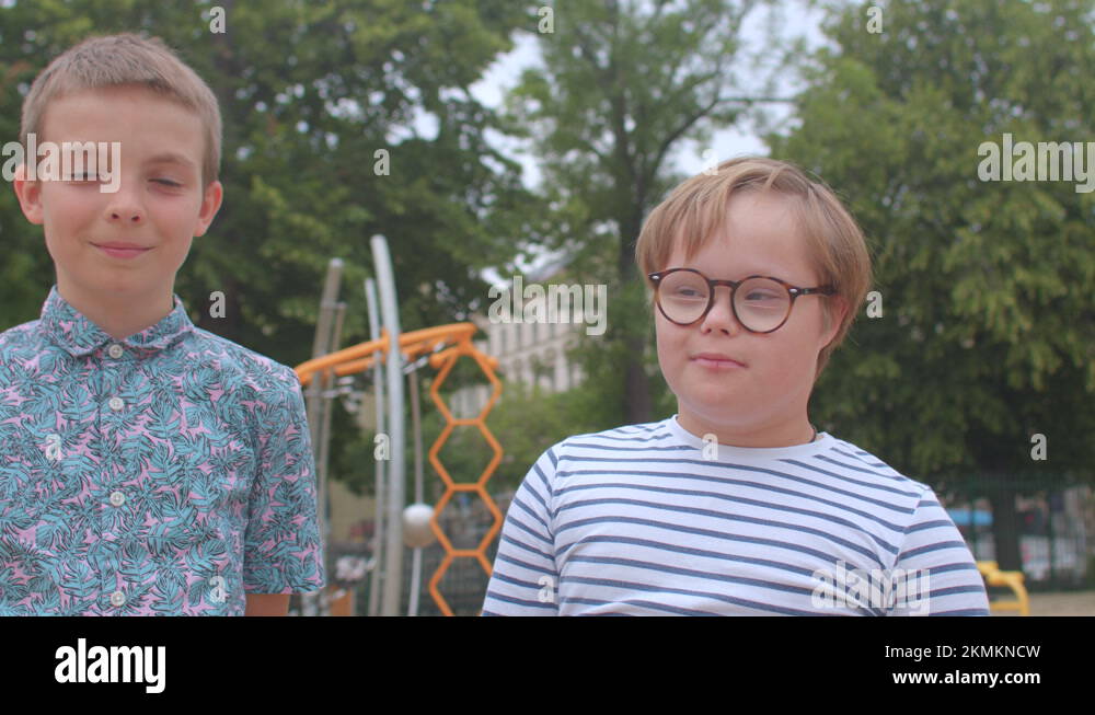 A teenager helps a boy with down syndrome to put on glasses Close