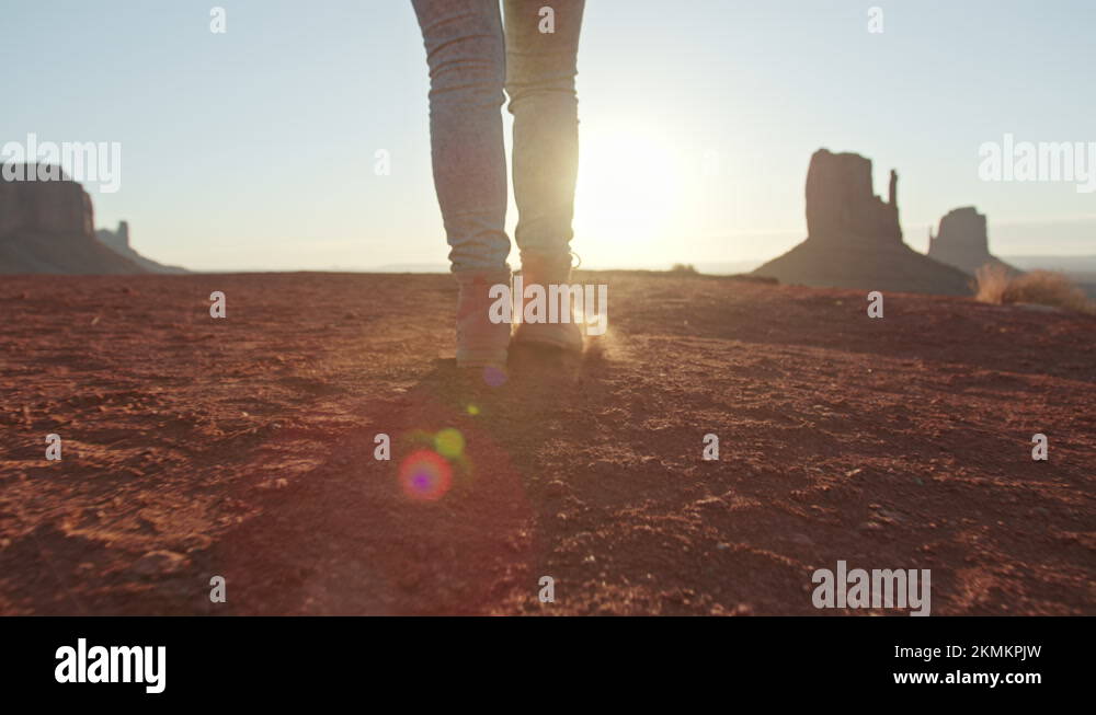 Woman feet walking in hiking boots in desert at golden sunset or