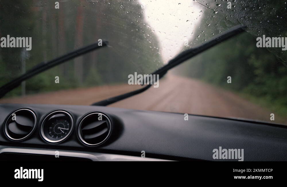 Car dashboard and front window with working wipers on the road in rainy ...