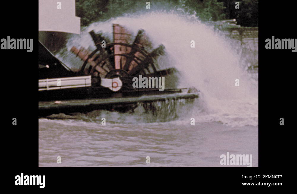 1970s Paddle wheel on back of riverboat turns. Man pilots boat