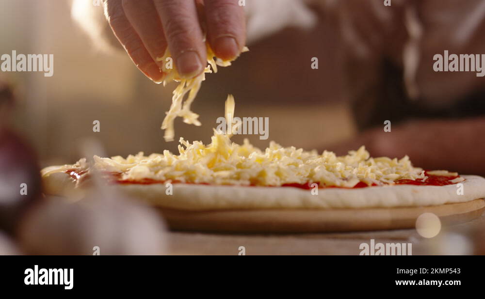 Close up shot of chef putting shredded cheese on pizza dough with