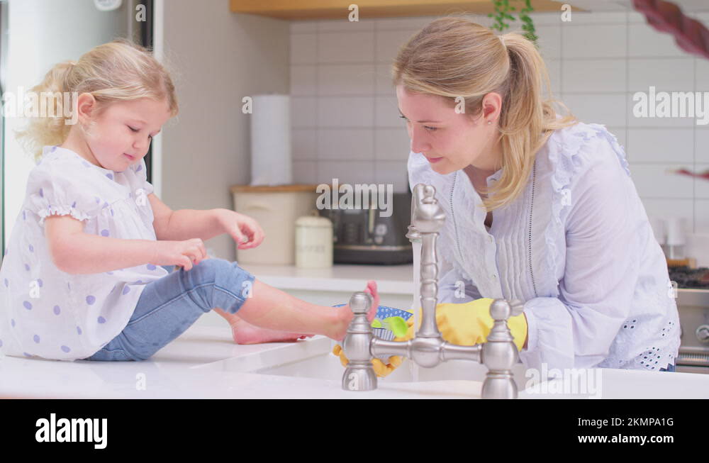 Mother wearing rubber gloves at home in kitchen with young daughter