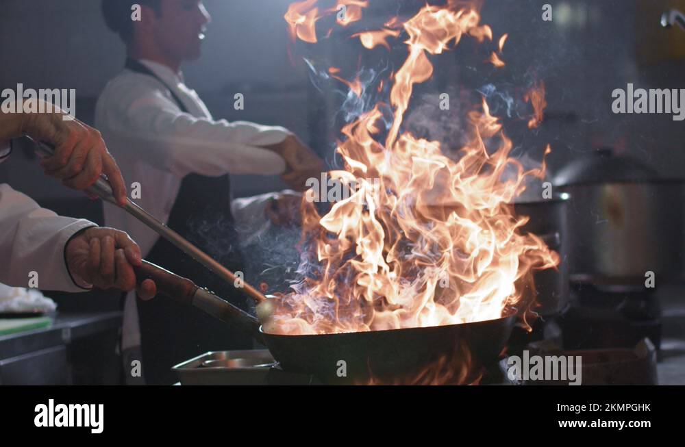Chefs cooking wok noodles in a skillet with tossing and blazing fire