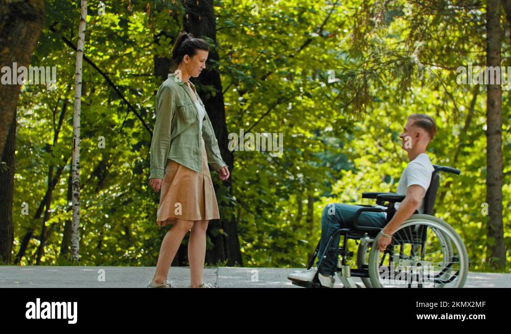 Disabled man in a wheelchair rides to his female friend and hugging her ...