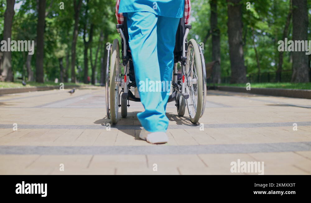 Feet of nurse walking and pushing wheelchair with patient, retirement