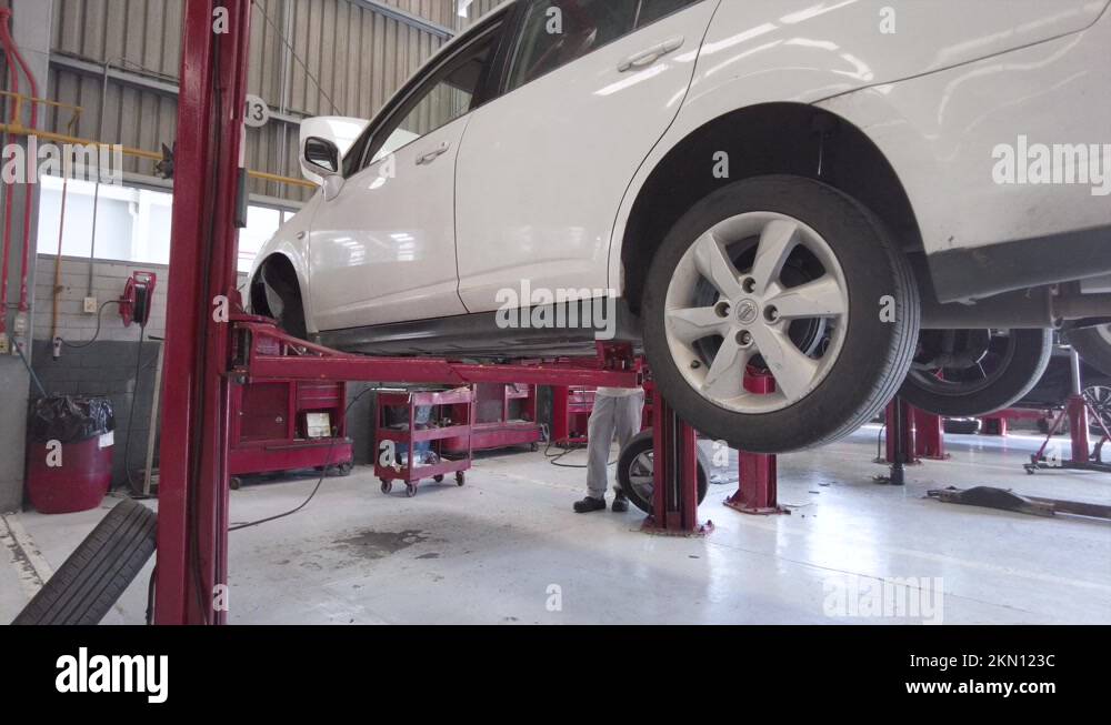 Lowering of a white car on a red car lift at a station garage